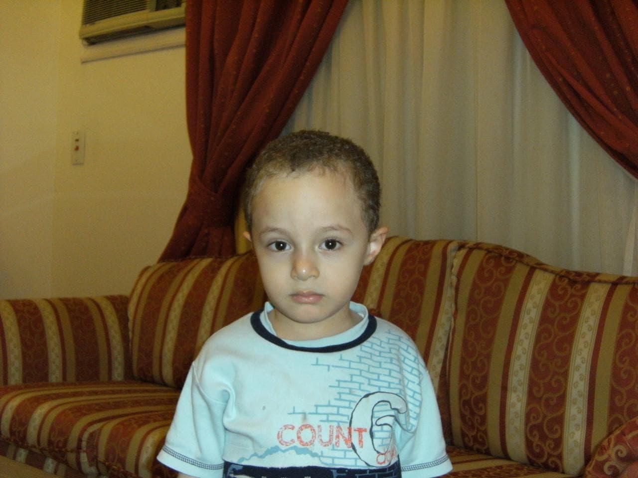 Me as a small child, sitting on a patterned sofa.